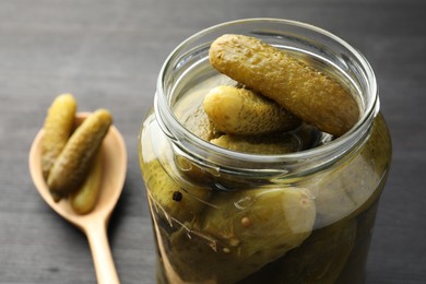 Jar and spoon with pickled cucumbers on grey wooden table, closeup