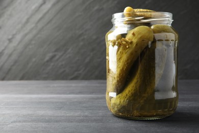 Photo of Pickled cucumbers in jar on grey wooden table. Space for text