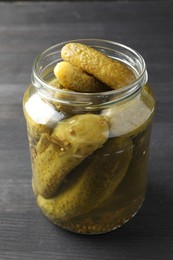 Pickled cucumbers in jar on grey wooden table