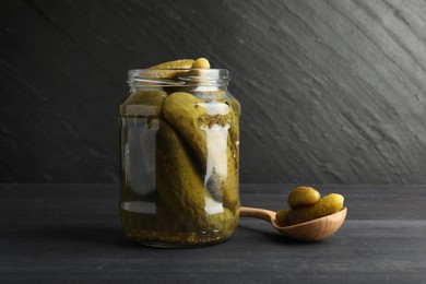 Photo of Jar and spoon with pickled cucumbers on grey wooden table