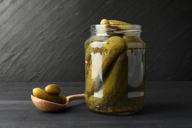 Photo of Jar and spoon with pickled cucumbers on grey wooden table