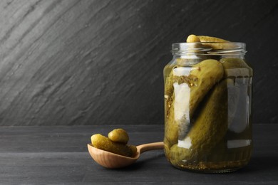 Photo of Jar and spoon with pickled cucumbers on grey wooden table. Space for text