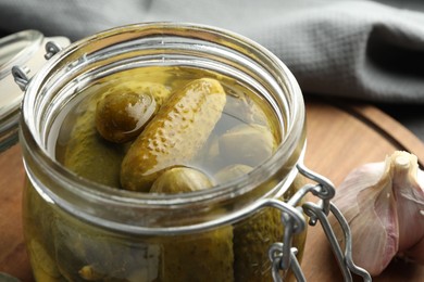 Photo of Pickled cucumbers in jar on wooden board, closeup