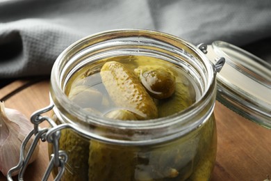 Photo of Pickled cucumbers in jar on wooden board, closeup