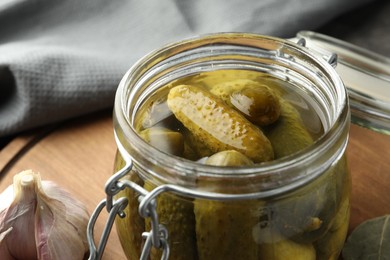 Photo of Pickled cucumbers in jar on wooden board, closeup