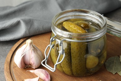 Pickled cucumbers in jar and spices on grey table