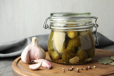Pickled cucumbers in jar and spices on grey table
