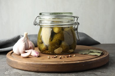 Photo of Pickled cucumbers in jar and spices on grey table