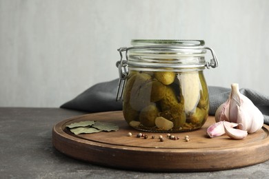 Photo of Pickled cucumbers in jar and spices on grey table