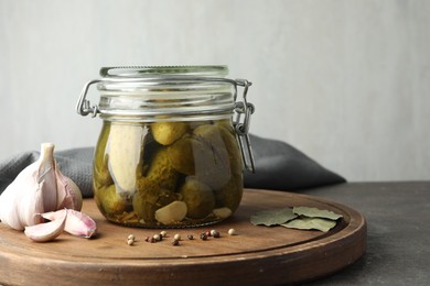 Pickled cucumbers in jar and spices on grey table