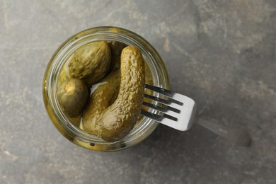 Photo of Taking pickled cucumber out of jar on grey table, top view