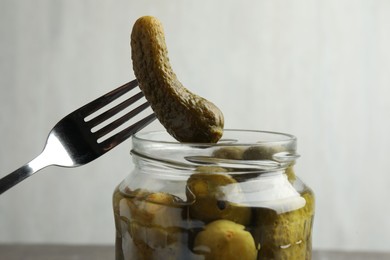 Photo of Taking pickled cucumber out of jar on grey background, closeup
