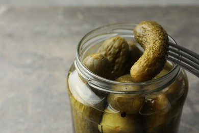 Photo of Taking pickled cucumber out of jar on grey background, closeup. Space for text