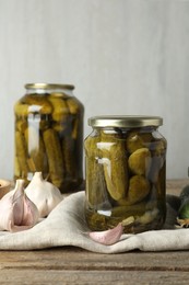 Photo of Pickled cucumbers in jars and garlic on wooden table