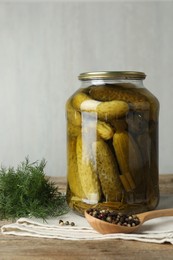 Pickled cucumbers in jar, dill and peppercorns on wooden table