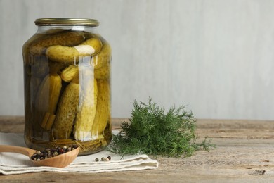Photo of Pickled cucumbers in jar, dill and peppercorns on wooden table. Space for text