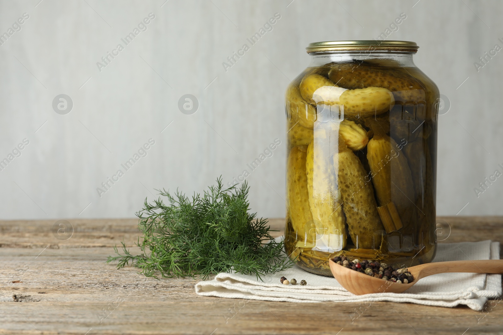 Photo of Pickled cucumbers in jar, dill and peppercorns on wooden table. Space for text