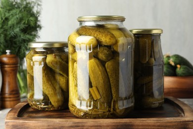 Pickled cucumbers in jars on wooden board