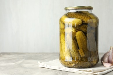 Photo of Pickled cucumbers in jar and garlic on grey table. Space for text