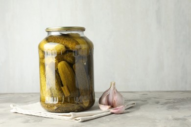 Photo of Pickled cucumbers in jar and garlic on grey table. Space for text