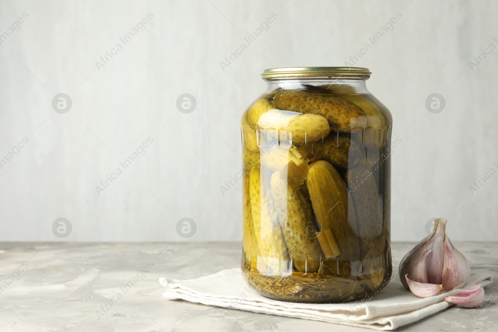 Photo of Pickled cucumbers in jar and garlic on grey table. Space for text