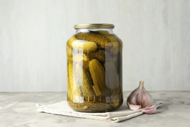 Pickled cucumbers in jar and garlic on grey table
