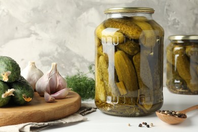 Pickles in jars, fresh cucumbers and spices on white table