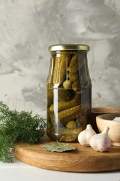 Pickled cucumbers in jar and spices on white table