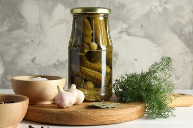 Pickled cucumbers in jar and spices on white table