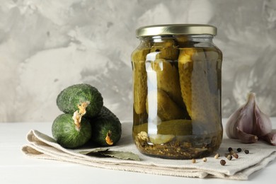 Pickles in jar, fresh cucumbers and spices on white table