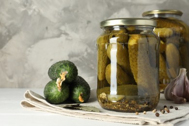 Pickles in jars, fresh cucumbers and spices on white table