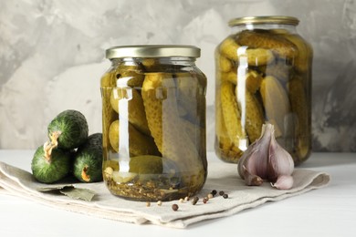 Pickles in jars, fresh cucumbers and spices on white table