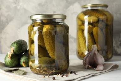 Pickles in jars, fresh cucumbers and spices on white table