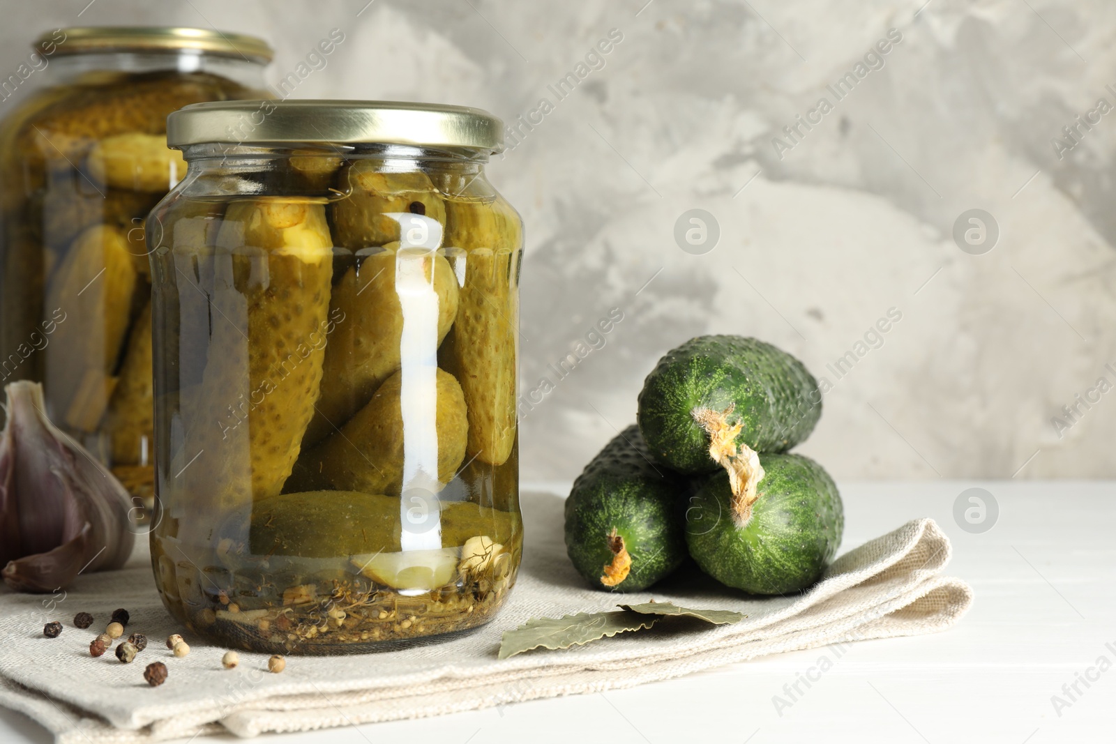 Photo of Pickles in jars, fresh cucumbers and spices on white table