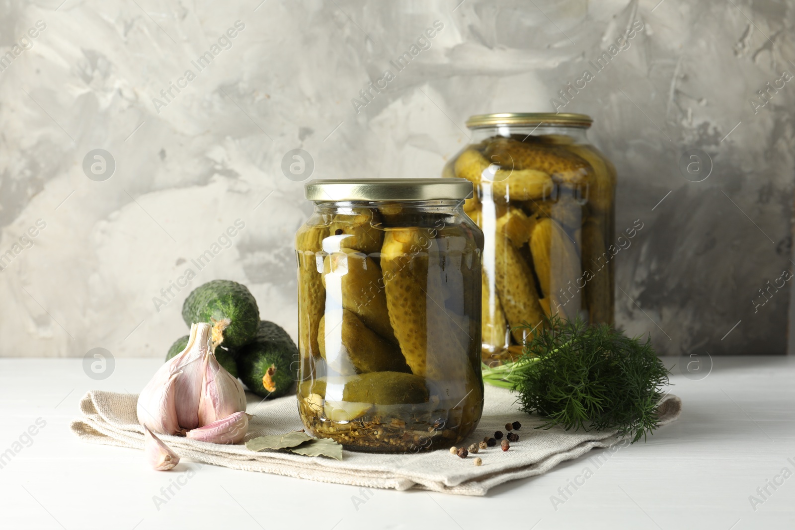 Photo of Pickles in jars, fresh cucumbers and spices on white table