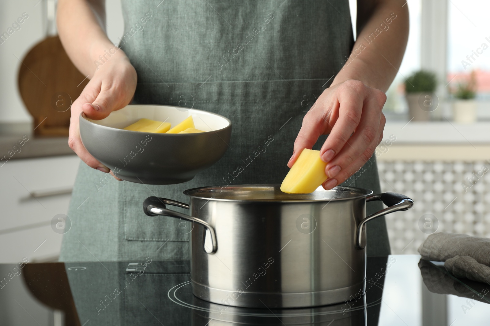 Photo of Woman putting potato into saucepan on stove, closeup