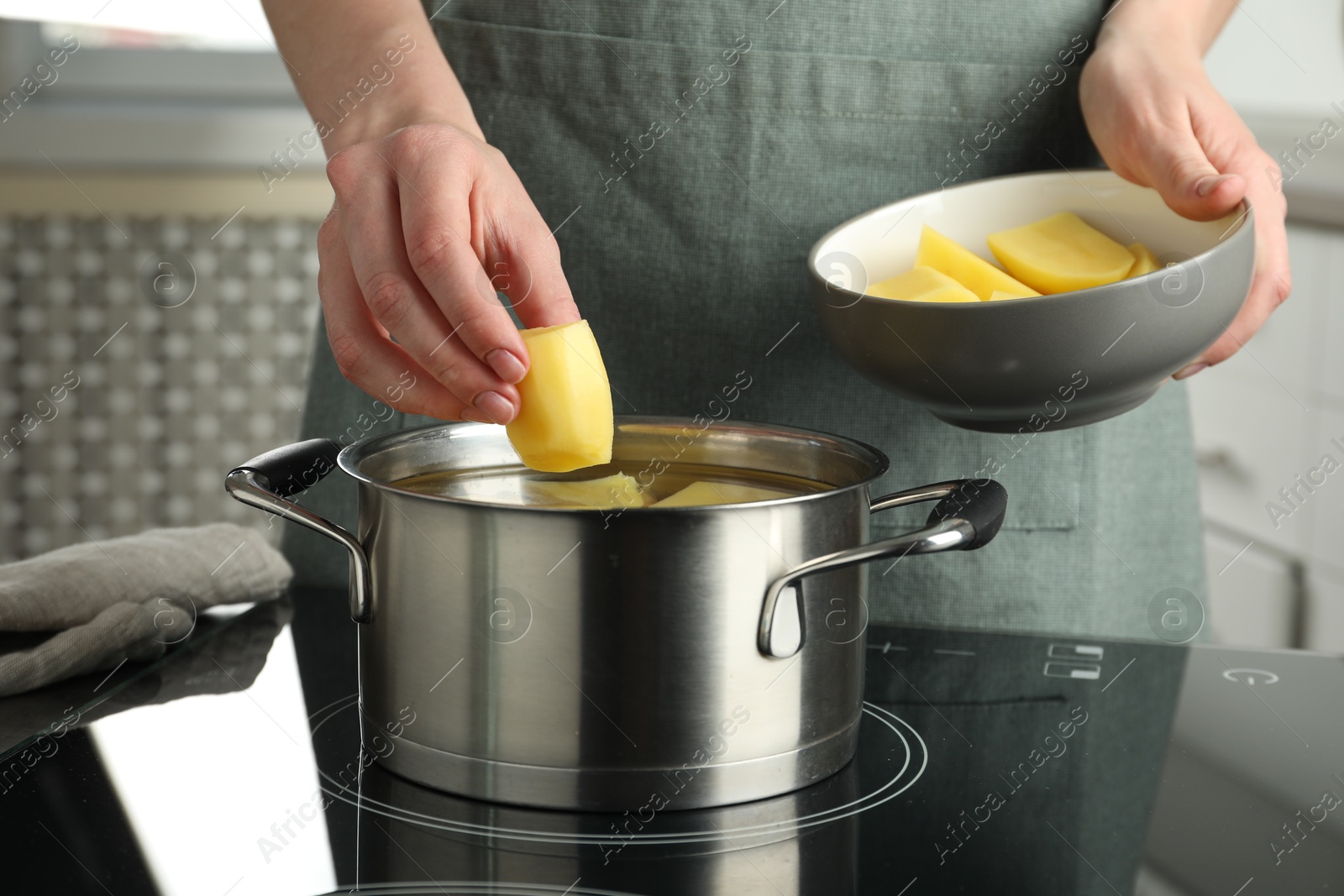 Photo of Woman putting potato into saucepan on stove, closeup