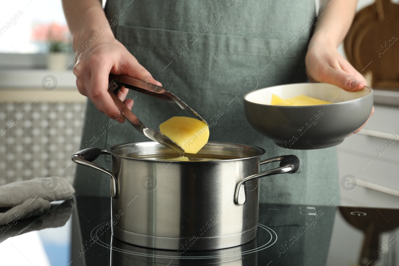 Photo of Woman putting potato into saucepan on stove, closeup