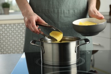 Woman putting potato into saucepan on stove, closeup