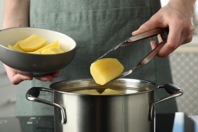 Photo of Woman putting potato into saucepan on stove, closeup