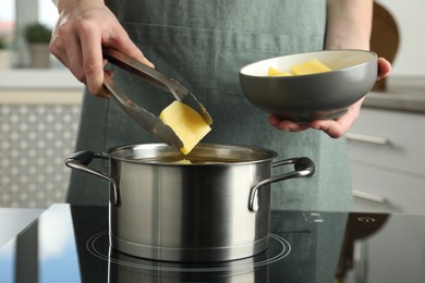 Photo of Woman putting potato into saucepan on stove, closeup