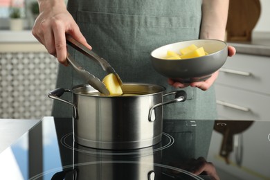 Woman putting potato into saucepan on stove, closeup