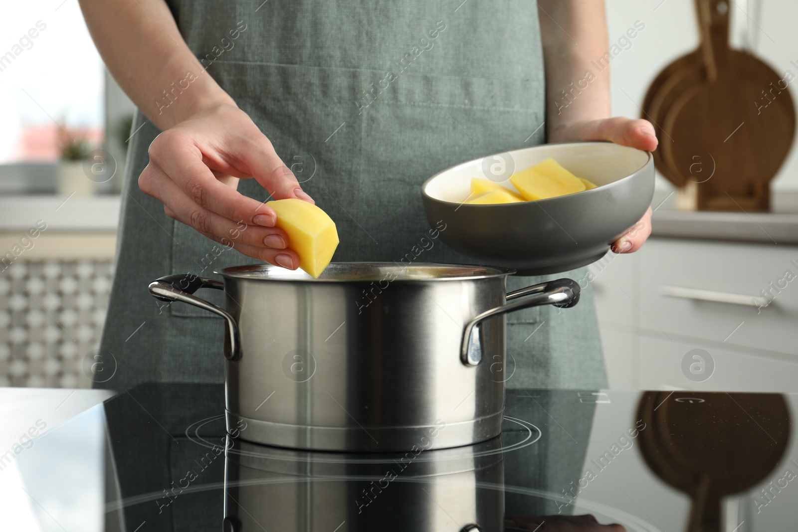 Photo of Woman putting potato into saucepan on stove, closeup