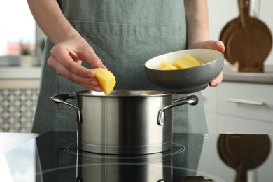 Woman putting potato into saucepan on stove, closeup