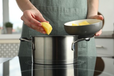 Photo of Woman putting potato into saucepan on stove, closeup