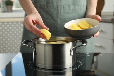 Photo of Woman putting potato into saucepan on stove, closeup