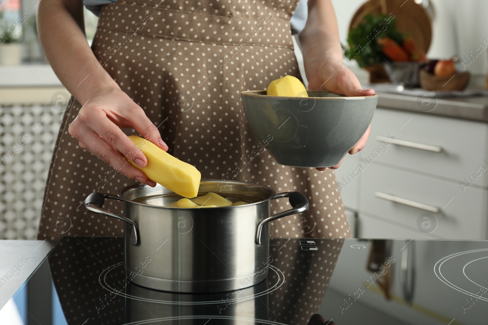 Photo of Woman putting potato into saucepan on stove, closeup