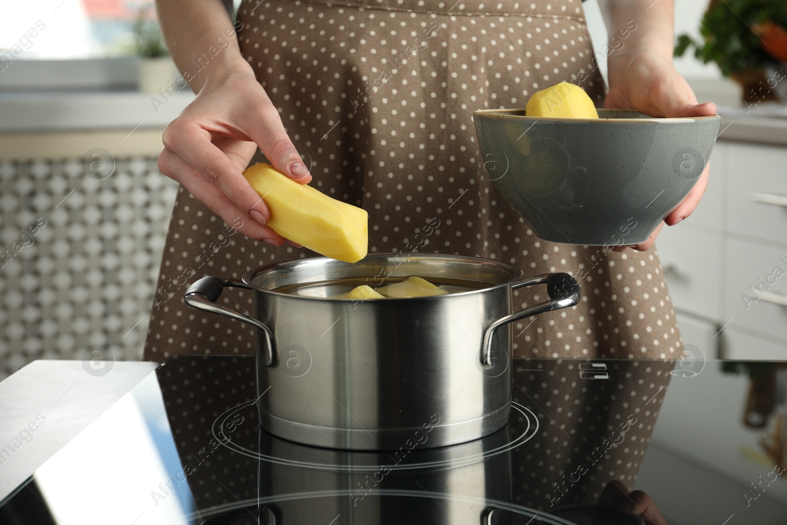 Photo of Woman putting potato into saucepan on stove, closeup