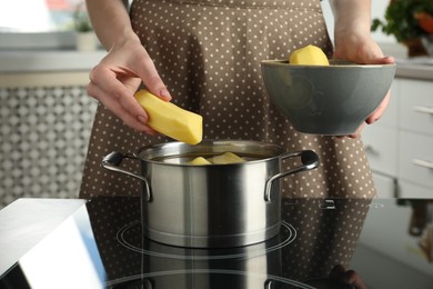 Woman putting potato into saucepan on stove, closeup