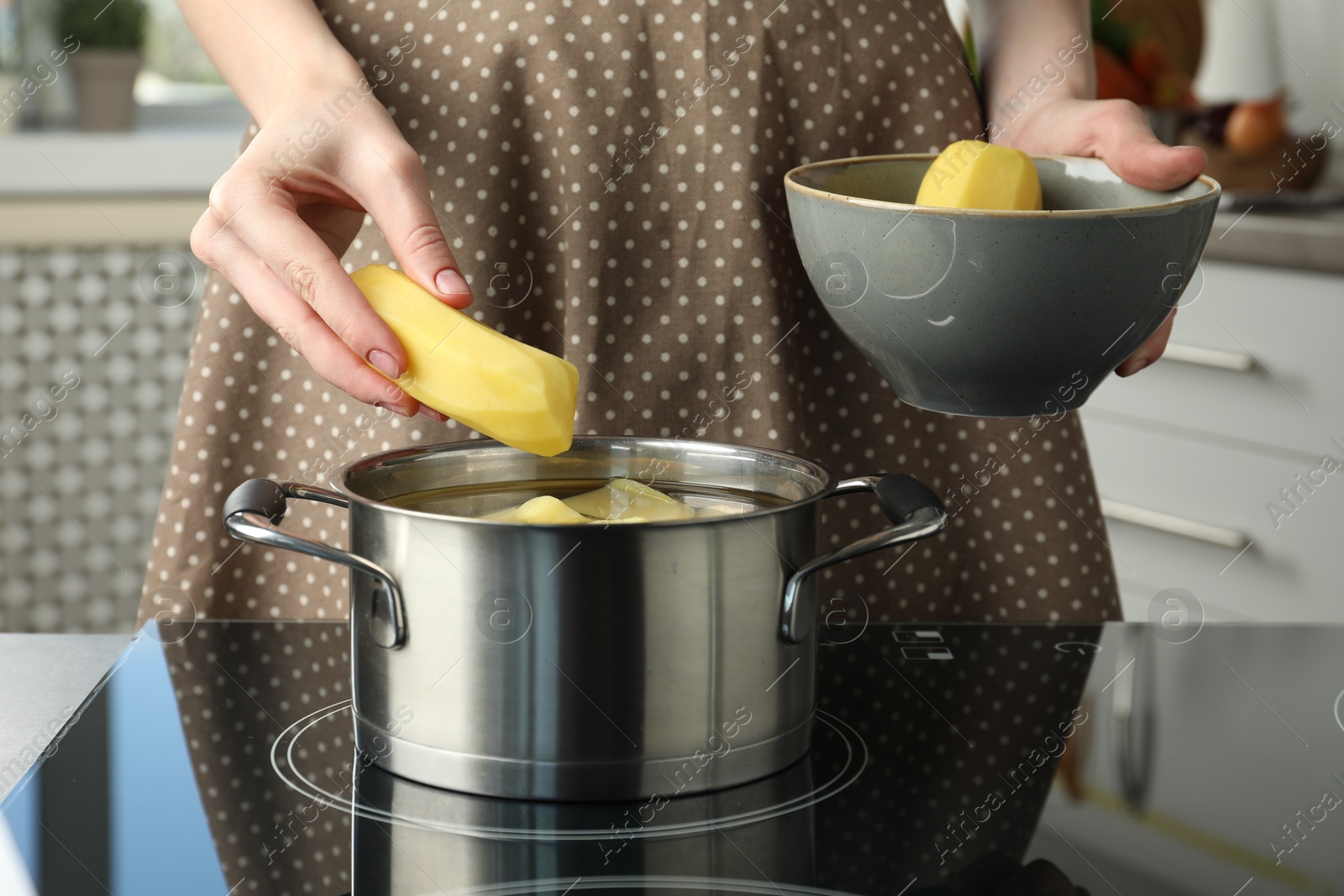 Photo of Woman putting potato into saucepan on stove, closeup